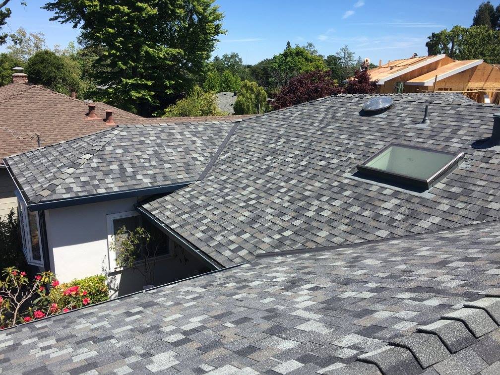 grey shingle roof installation with rectangular skylight in residential neighborhood